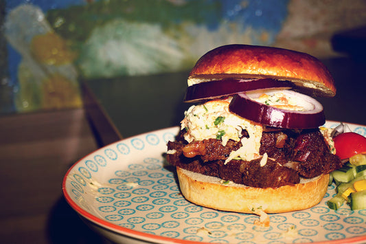 Hamburgare med grillat kött, rödlök och coleslaw på ett mönstrat fat, serverad med grönsaker.