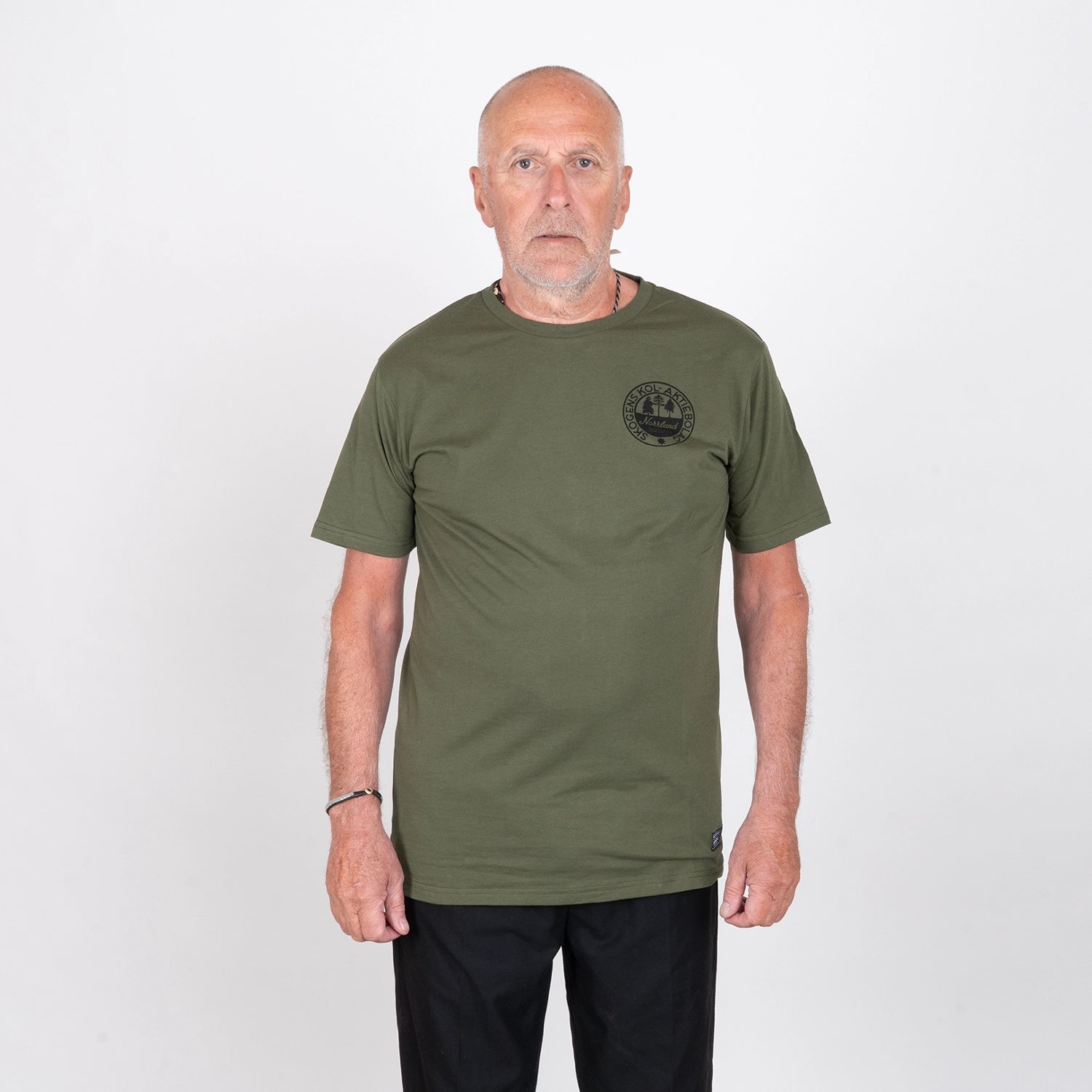 Man i olivgrön t-shirt med svart tryck, neutralt poserande mot vit bakgrund.
