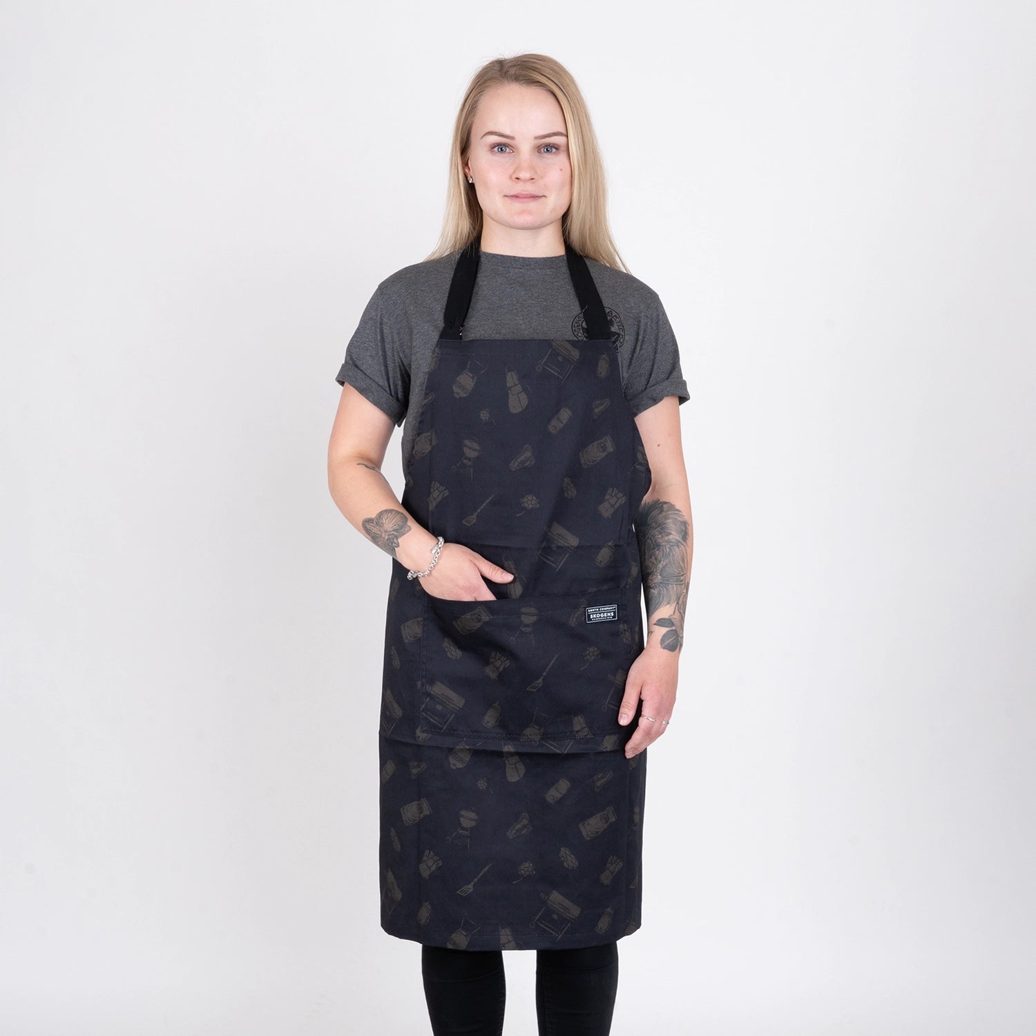Person med helsvart grillförkläde med grillmönster står mot vit bakgrund