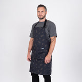 Man i grå t-shirt bär svart grillförkläde, perfekt för utomhusmatlagning och BBQ.