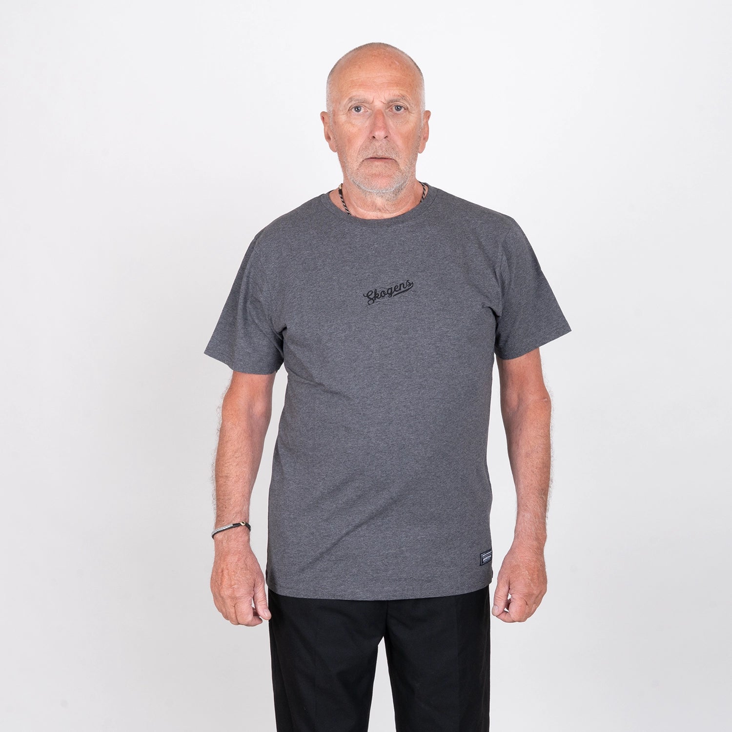 Äldre man i mörkgrå t-shirt med tryck, stående mot vit bakgrund, grillkläder.