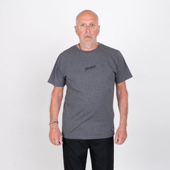 Äldre man i mörkgrå t-shirt med tryck, stående mot vit bakgrund, grillkläder.