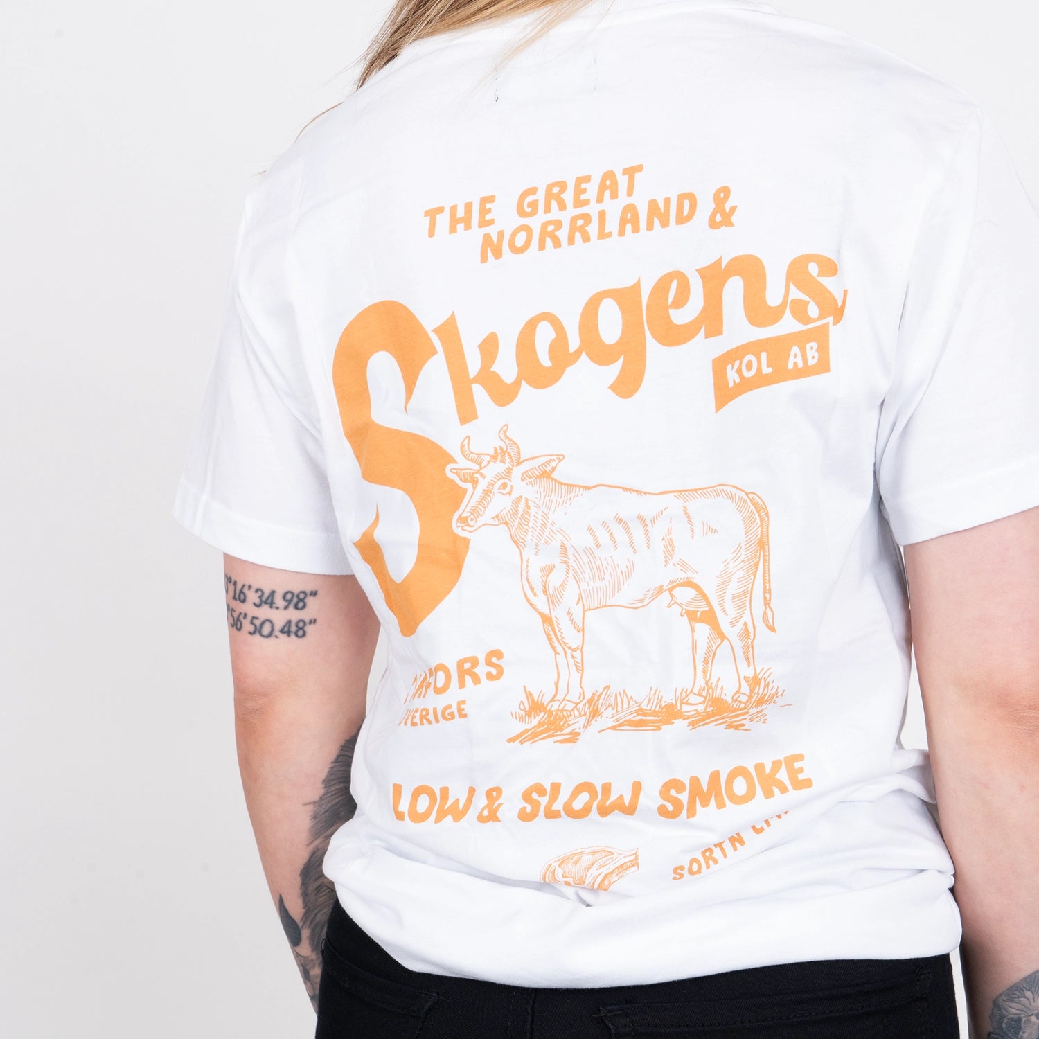 Vit T-shirt med orange tryck av ko och grilltema, person sedd bakifrån.