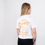 Kvinna i vit t-shirt med orange tryck, motiv av ko och text om Norrland och grillning.