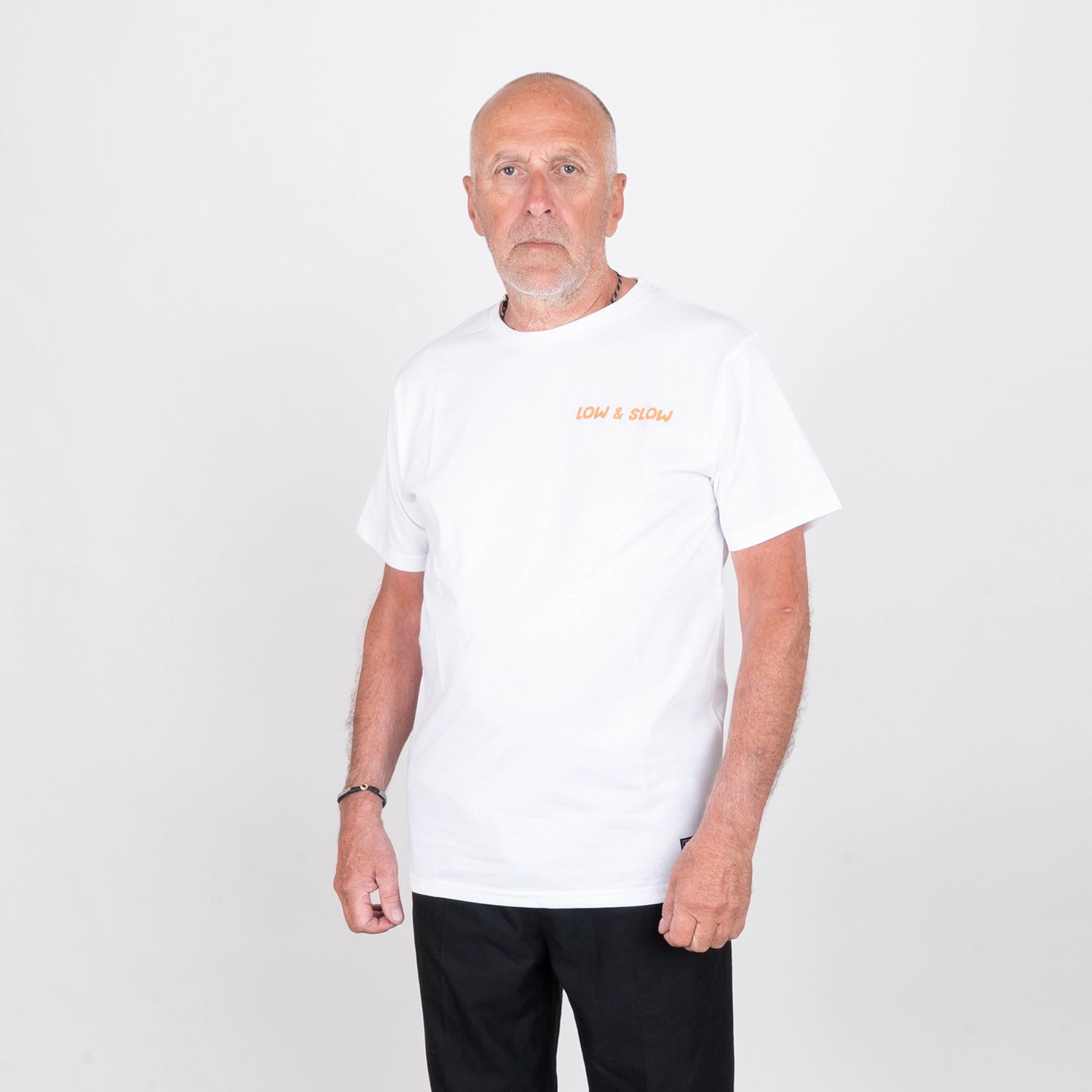 Man i vit t-shirt med texten 'LOW & SLOW', poserar mot vit bakgrund.