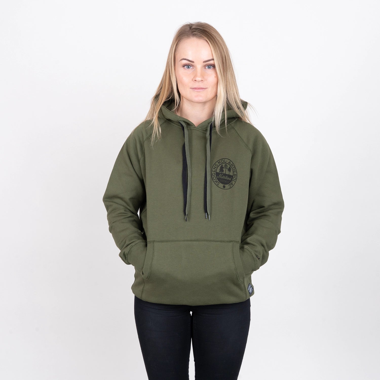 Kvinna i olivgrön hoodie med tryck, händer i fickorna, neutralt bakgrund, modekläder