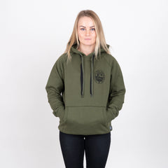 Kvinna i olivgrön hoodie med tryck, händer i fickorna, neutralt bakgrund, modekläder