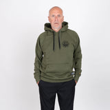 Man i olivgrön hoodie med tryckt logotyp, stående mot vit bakgrund.