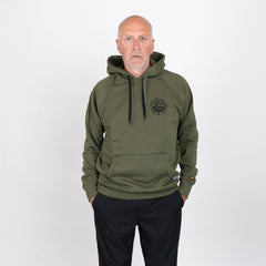 Man i olivgrön hoodie med tryckt logotyp, stående mot vit bakgrund.