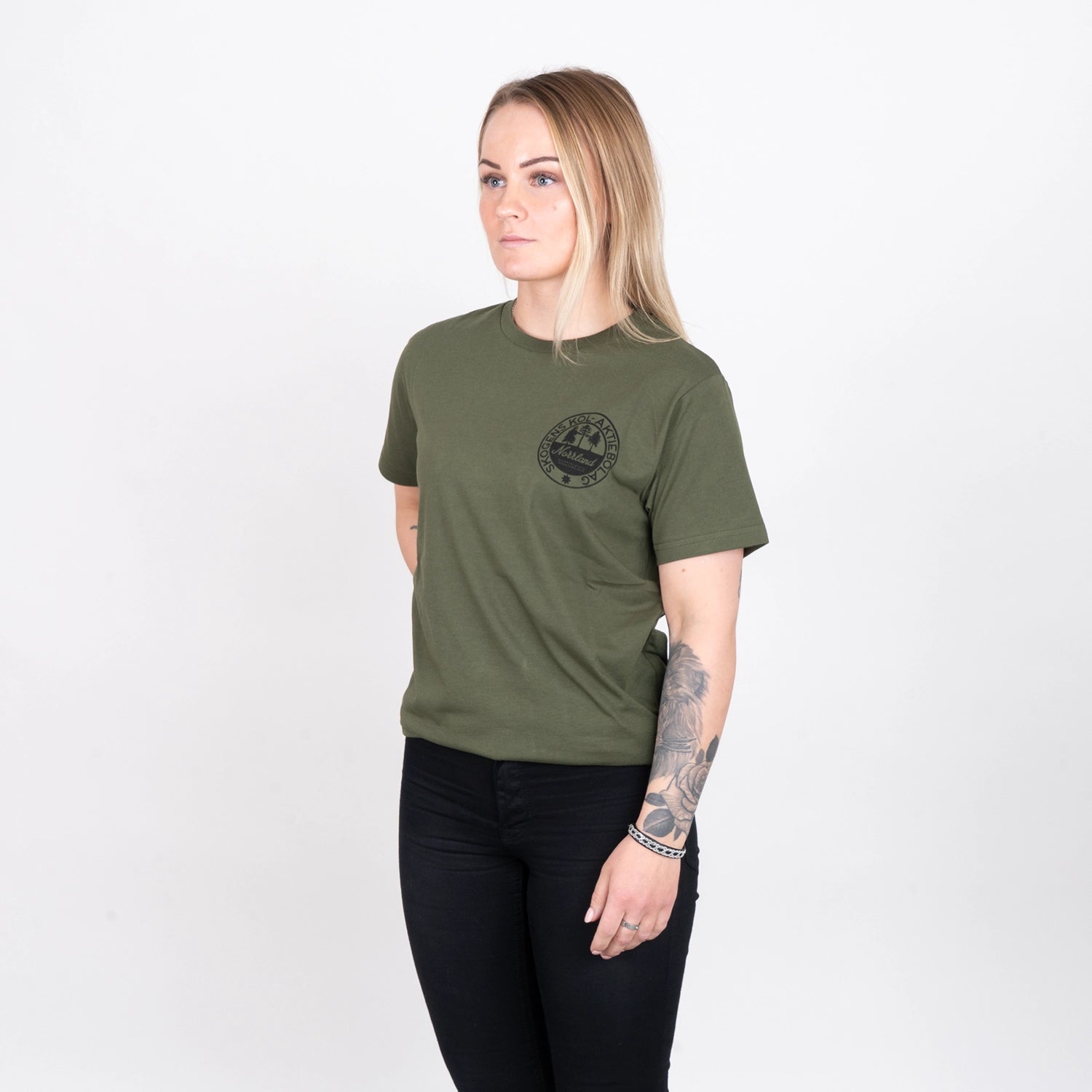 Kvinna i olivgrön t-shirt med tryck, svarta byxor, vit bakgrund