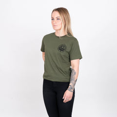 Kvinna i olivgrön t-shirt med tryck, svarta byxor, vit bakgrund
