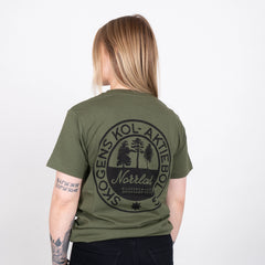 Person i grön t-shirt med svart tryck, text och skogsmotiv på ryggen, grillrelaterad.