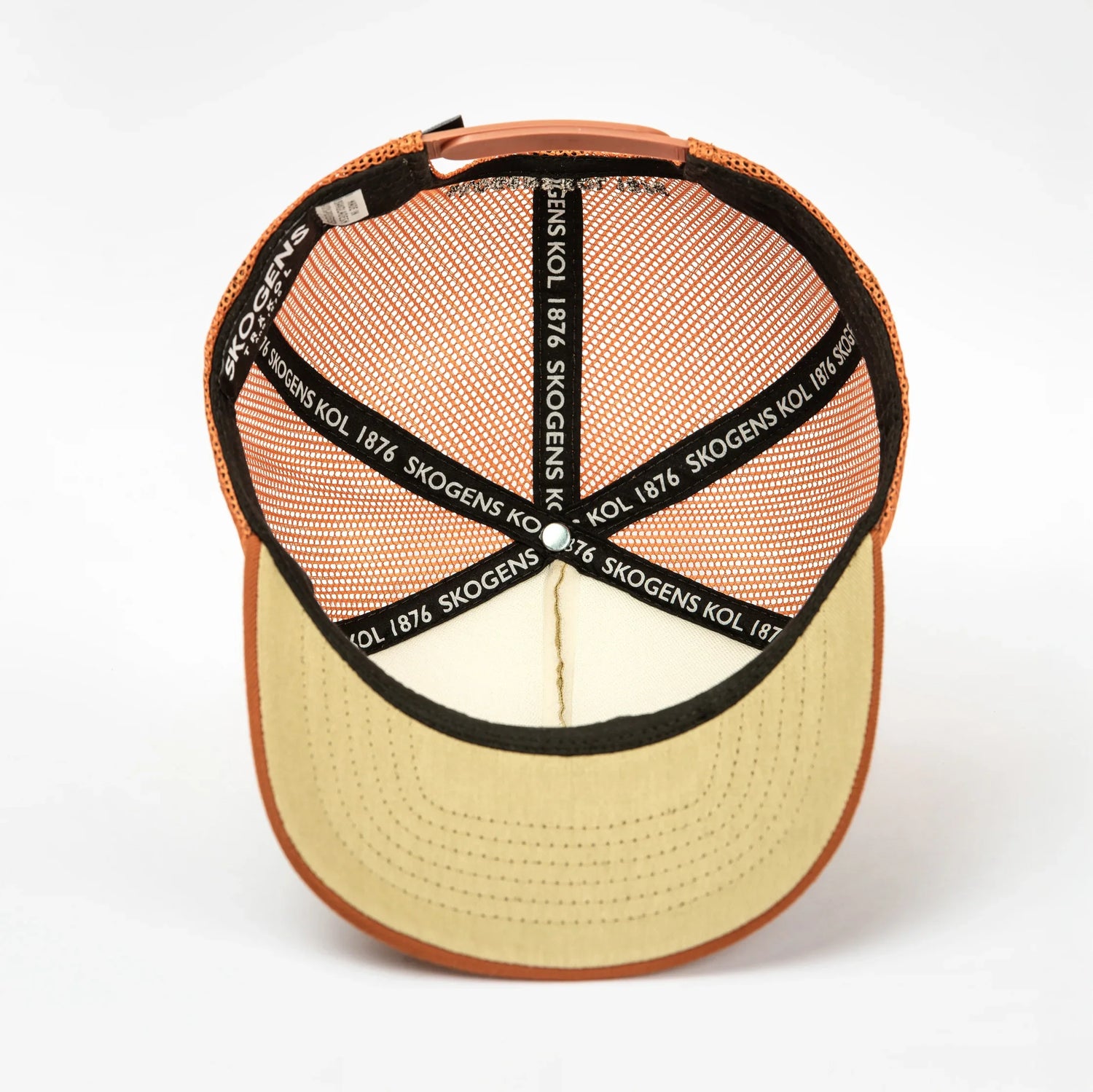 Insidan av orange och beige keps med svart nät och texten 'SKOGENS KOL 1876' på banden.