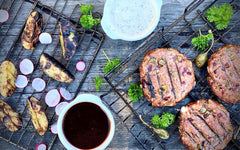 Grillade hamburgare med grillade potatisklyftor, rädisor, såser och persilja på grillgaller.